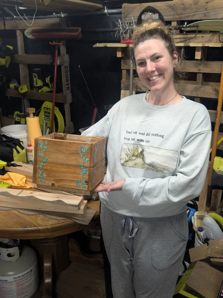Sydney in the workshop holding a wooden planter with colorful leaf decoration